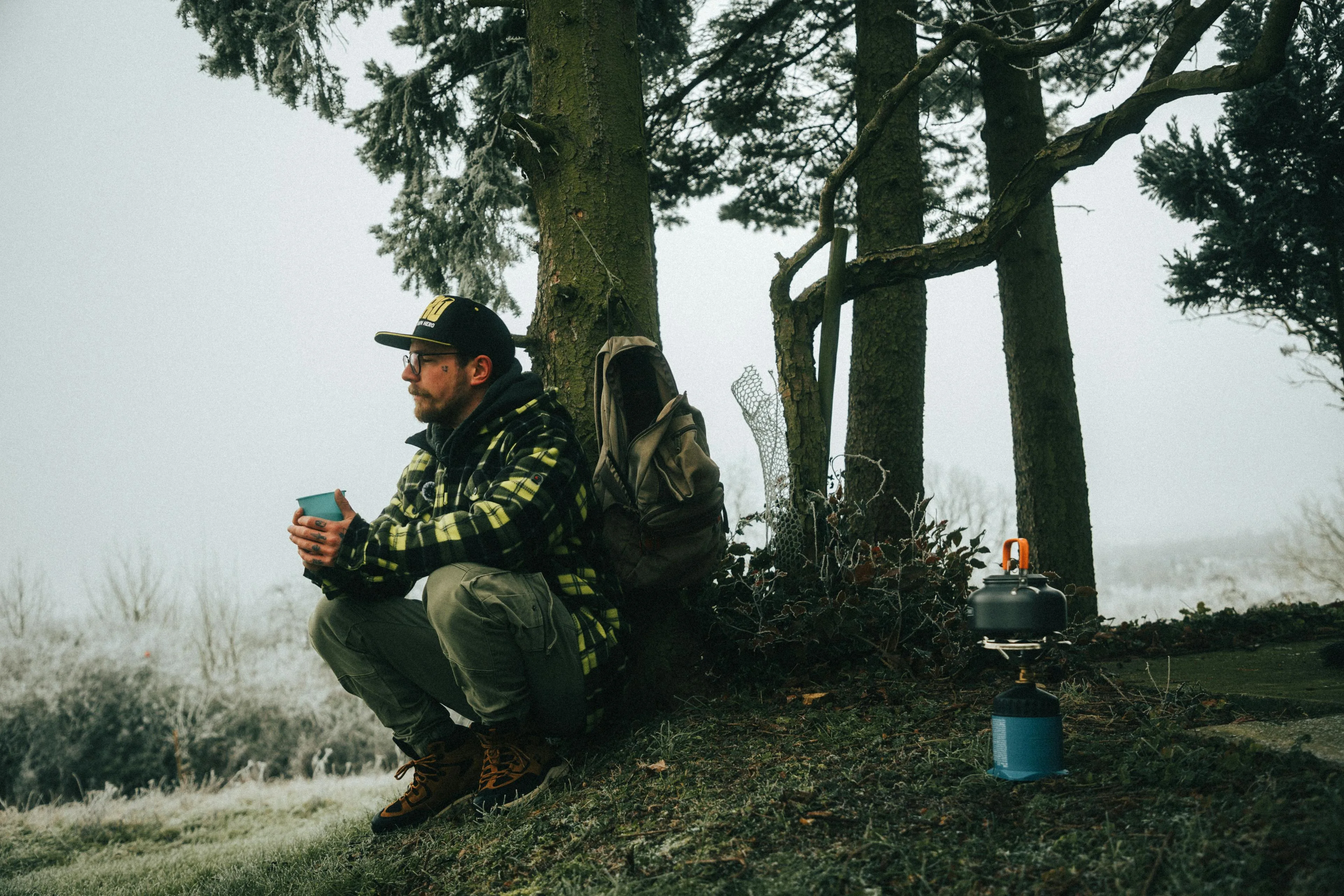 Camper in layered outdoor clothing enjoying a warm drink in a frosty winter forest