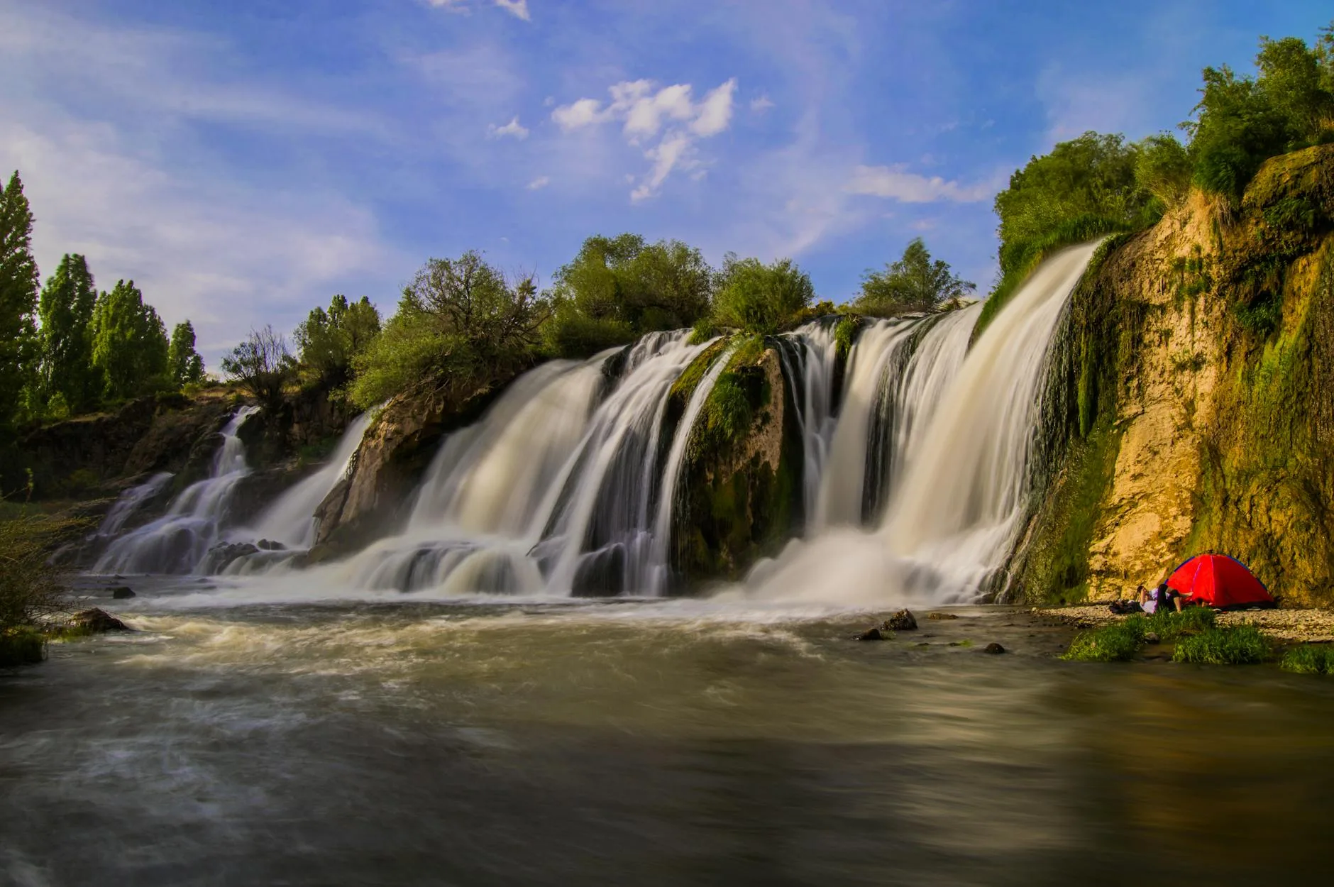Tent set up near a clear stream surrounded by trees and nature