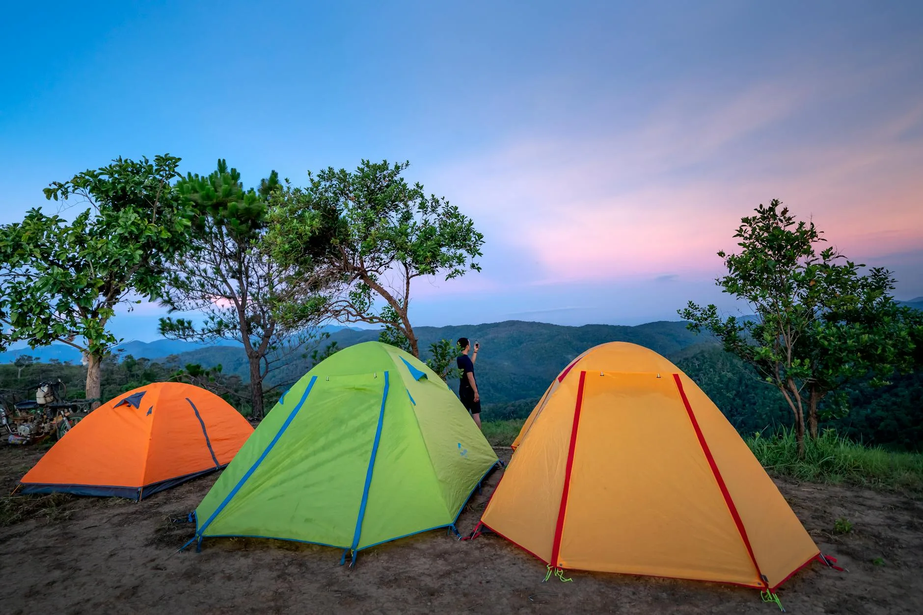 Colourful tents pitched on a hilltop ridge with forested mountains at sunset