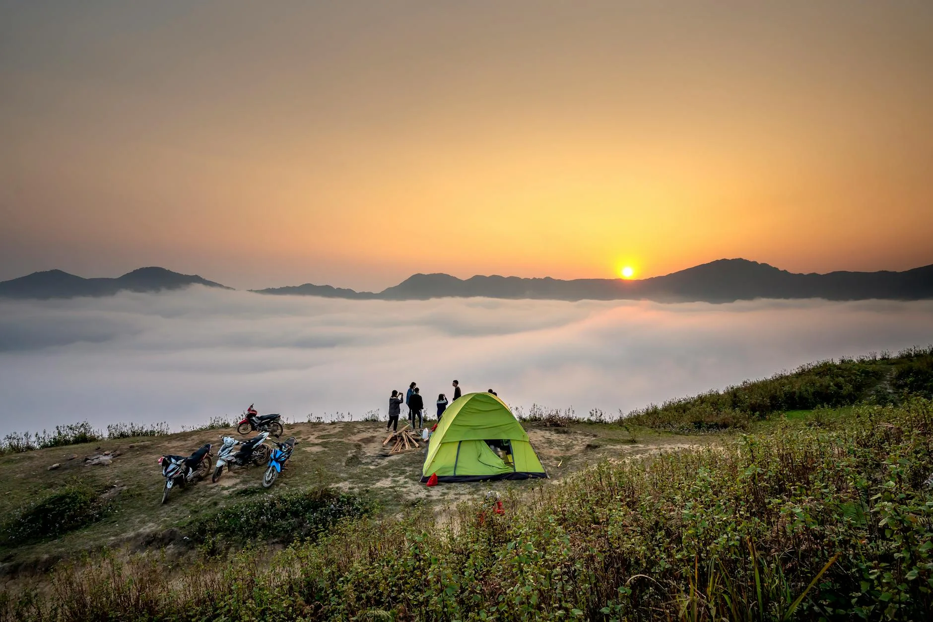 Tent on a mountain summit at sunrise above a sea of clouds