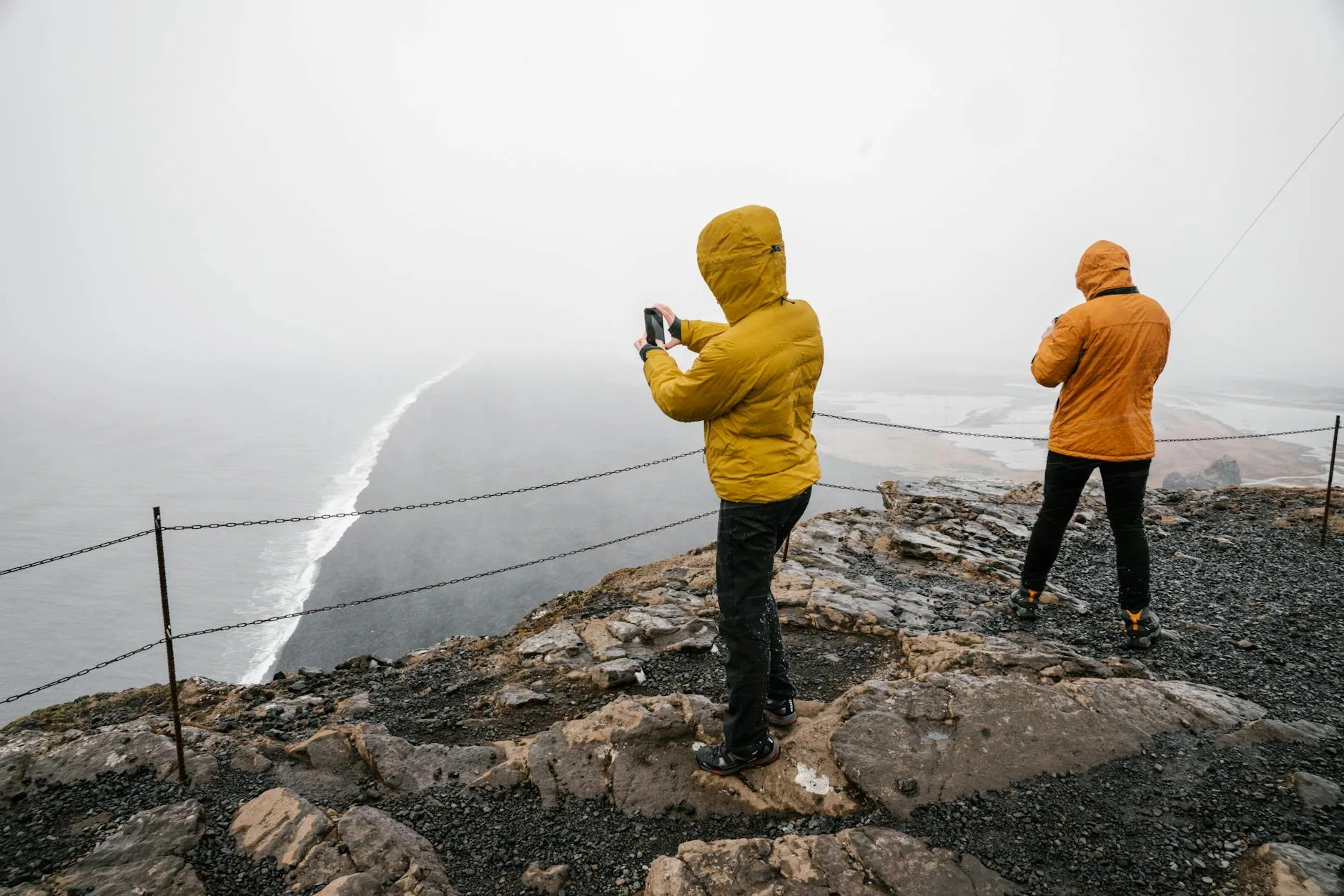 Two hikers wearing yellow waterproof jackets on a misty coastline