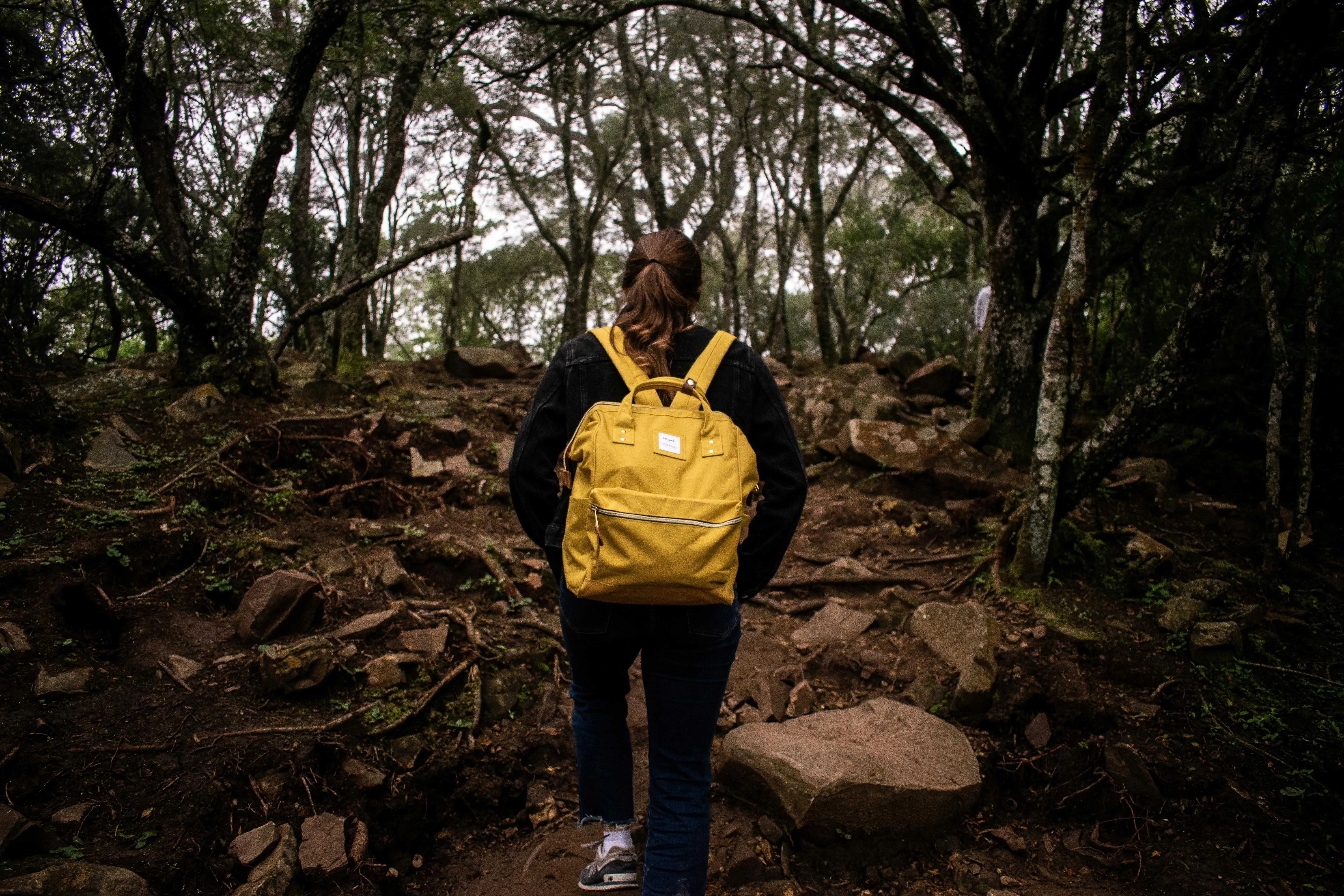 Woman hiking up a woodland trail wearing a bright yellow rucksack