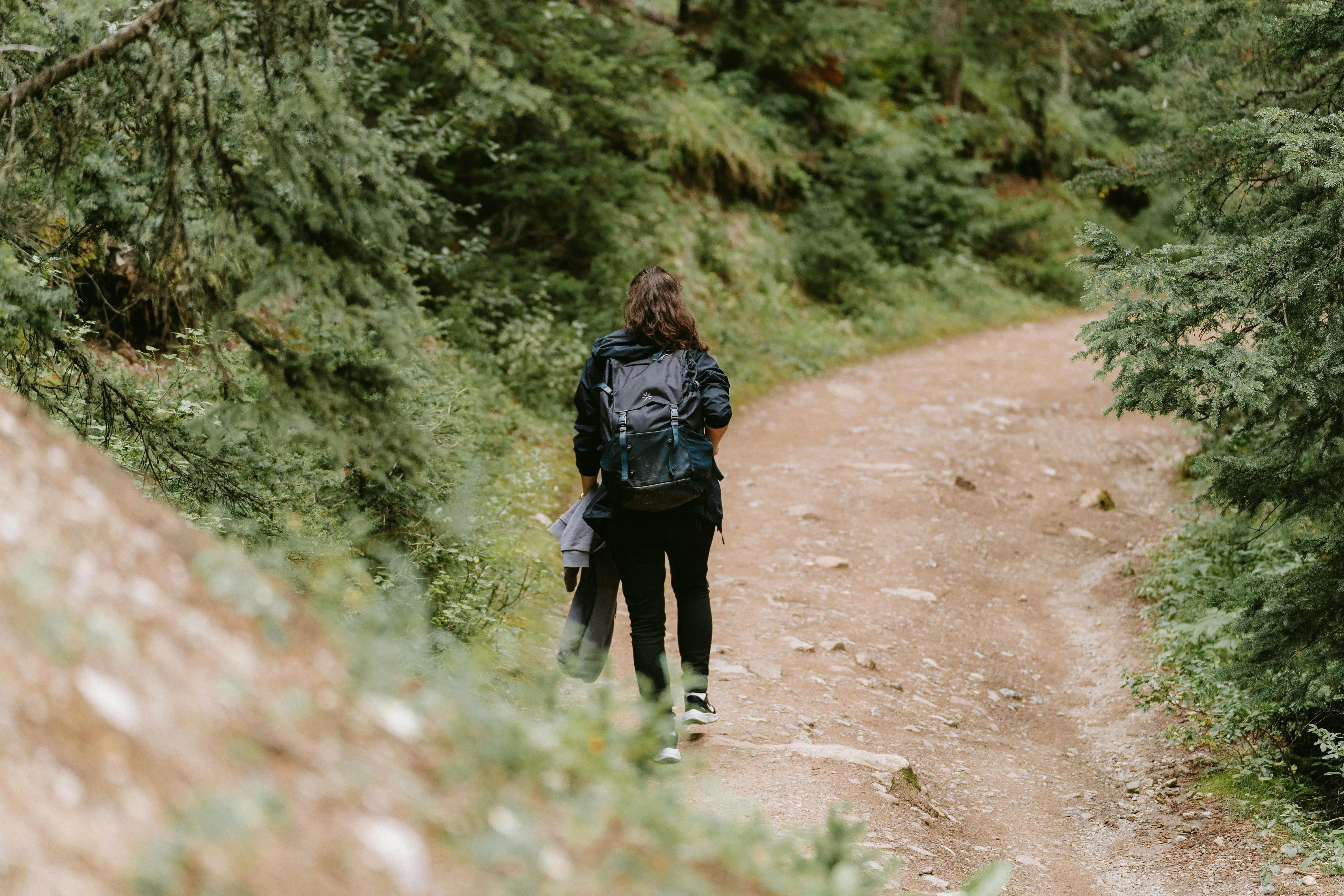 Woman walking along a forest trail with a dark hiking rucksack