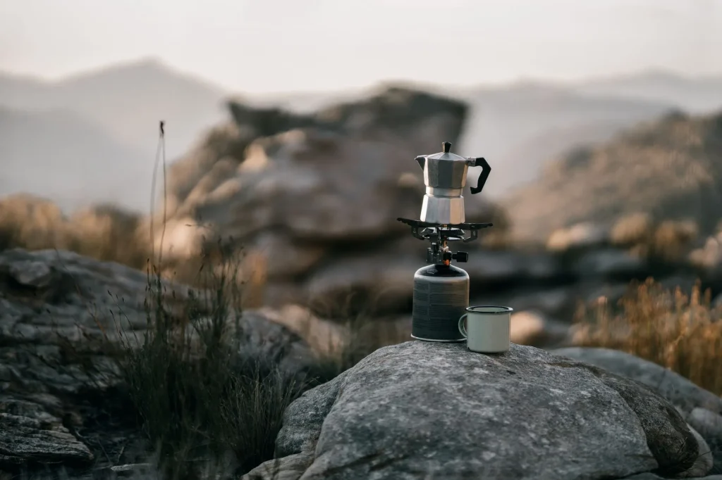 Coffee brewing beside a camping stove outdoors